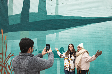 A couple of girls taking a picture in front of the Sanctuary mural in downtown Eau Claire in the winter 