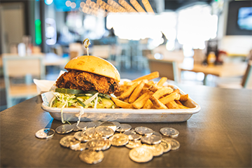 A chicken sandwich and french fries sitting on a tray on a table next to some arcade tokens and the Reboot Social in Eau Claire, Wisconsin 