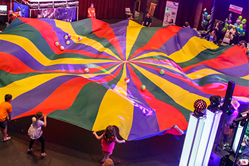 a bunch of kids playing with a colorful parachute at the Great Hullabaloo in Eau Claire 