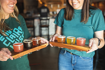 Two women carrying flights of beer at Modicum 