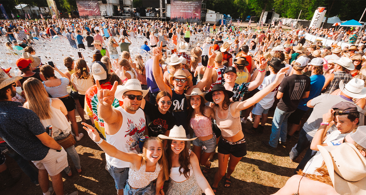 A group of friends posing for a photo in front of the Country Jam mainstage 