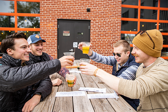 A group of 4 friends cheers their beers on the outdoor patio at The Brewing Projekt 