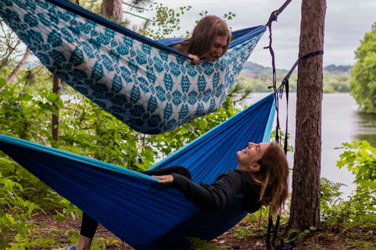 two girls in hammocks that are stacked on top of each other in the trees, laughing while enjoying the view in Eau Claire