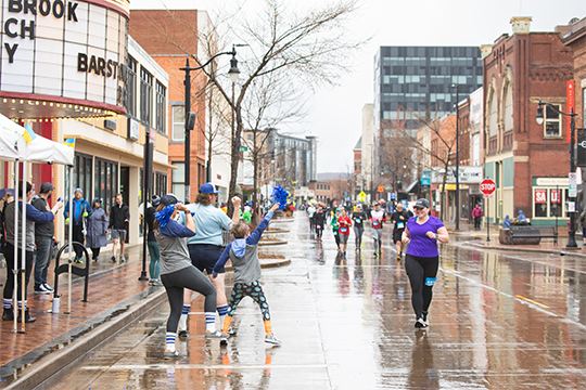 a girl running down barstow street  while the crowd cheers her on at the eau claire marathon 