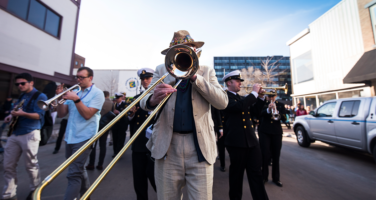 a man wearing a tan suit and hat playing a trombone on Barstow Street in Eau Claire 